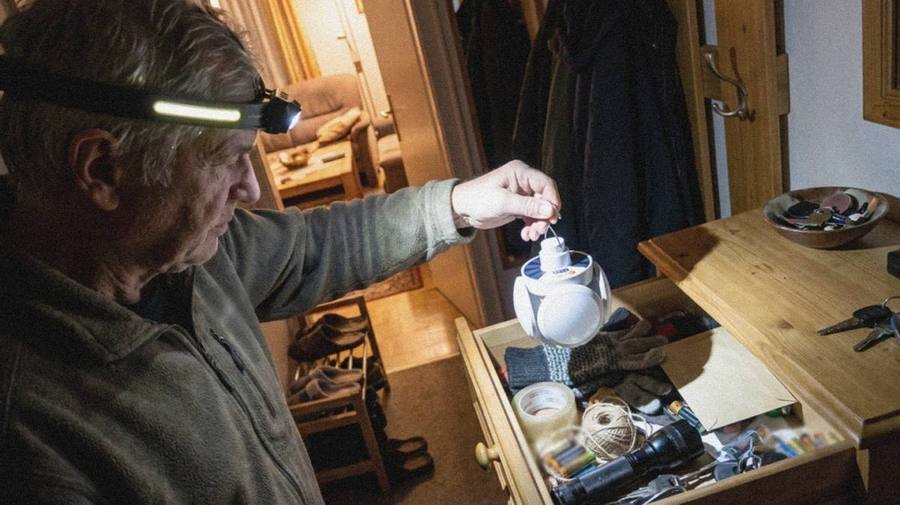 Älterer Mann mit eingeschalteter Stirnlampe holt eine Leuchte aus einer Schublade im dunklen Flur