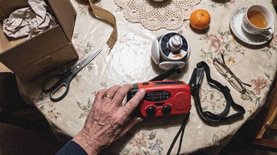 Die drei Geräte des Notfallsets von oben auf einem Tisch: rotes Kurbelradio, faltbare LED-Leuchte und Stirnlampe